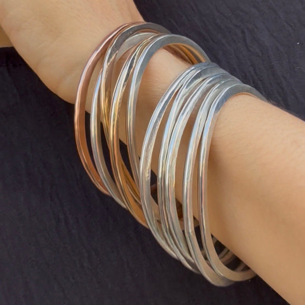Orbit bangle set in rose-gold, gold, and silver—hand-forged stacking bracelets with sculptural form by Elke Van Dyke.