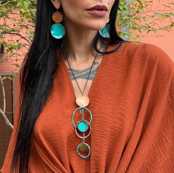 The Blue Hole Necklace by Elke Van Dyke Design. A turquoise and orange copper necklace displayed on a black mannequin, featuring a series of linked circles and pendants.
