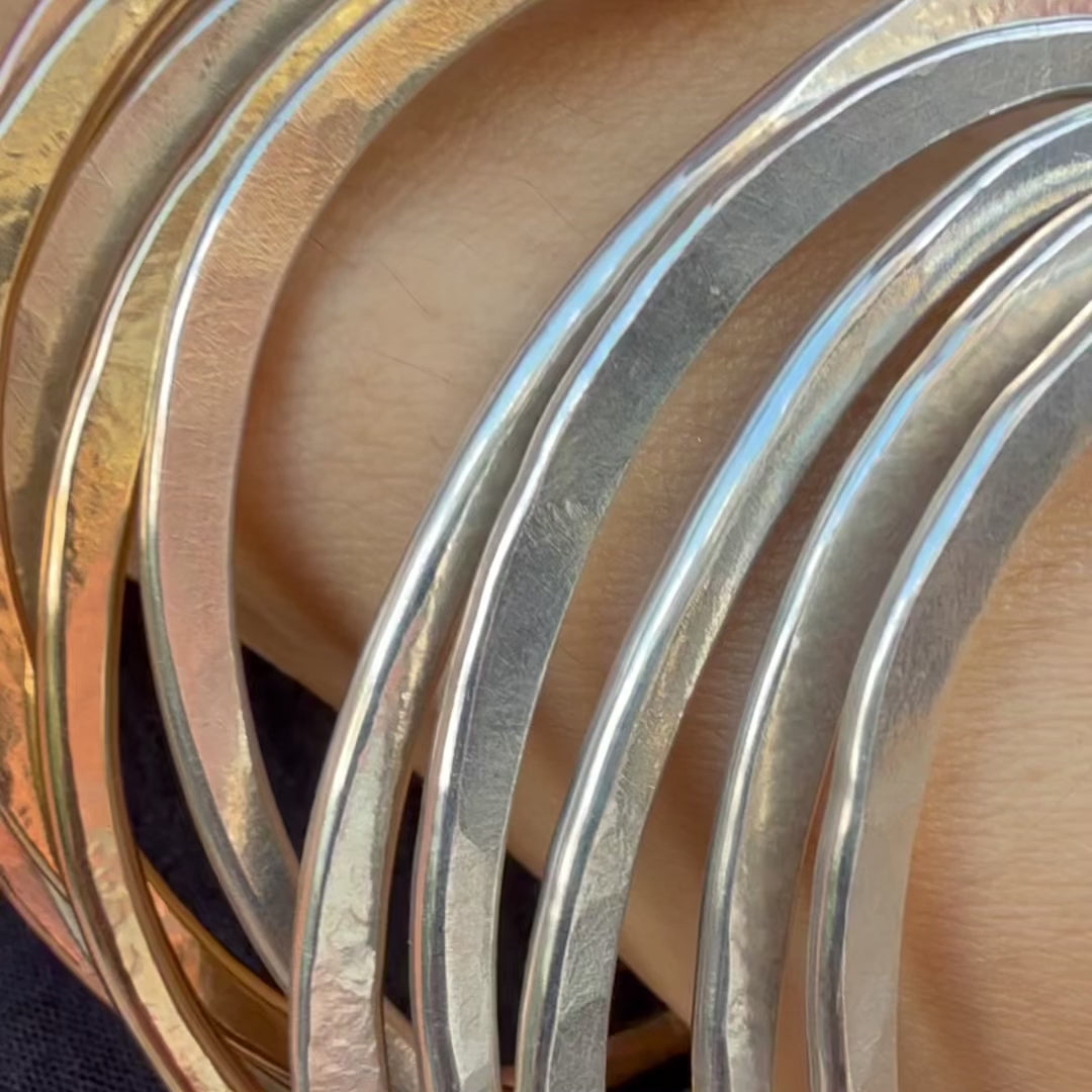 Video of Orbit bangle bracelets and earrings  in silver on model. Stackable forms, artisanal metal finishes by Elke Van Dyke.